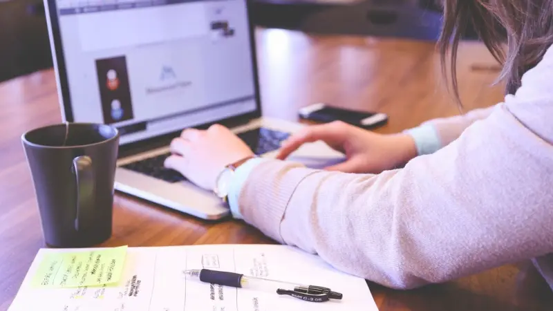 A professional working on a laptop with research notes