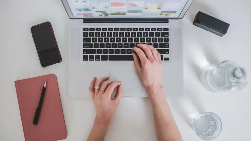 Working on a laptop at a desk with a notebook and phone