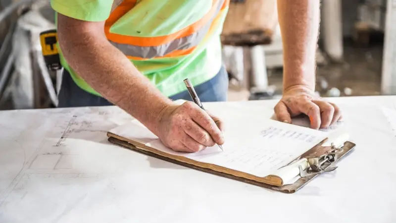 A tradesperson in a hi-vis vest checking building plans
